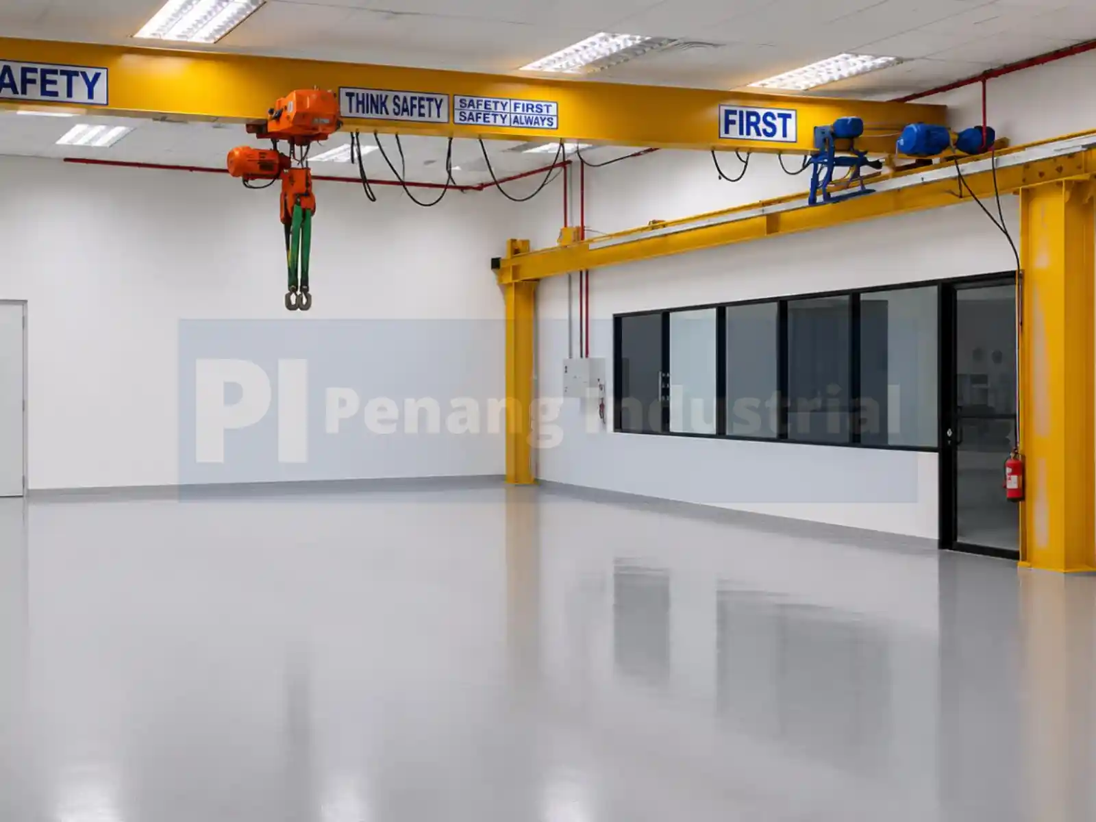 Interior production area of a factory for sale in Bayan Lepas featuring a heavy-duty yellow overhead crane, grey epoxy flooring, and a glass-partitioned office space.